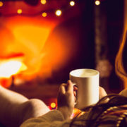 Toned photo of woman warming up with hot tea at fireplace at winter